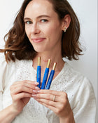 ELEUSIA founder Liz Farkas holding three blue lip products against a white background
