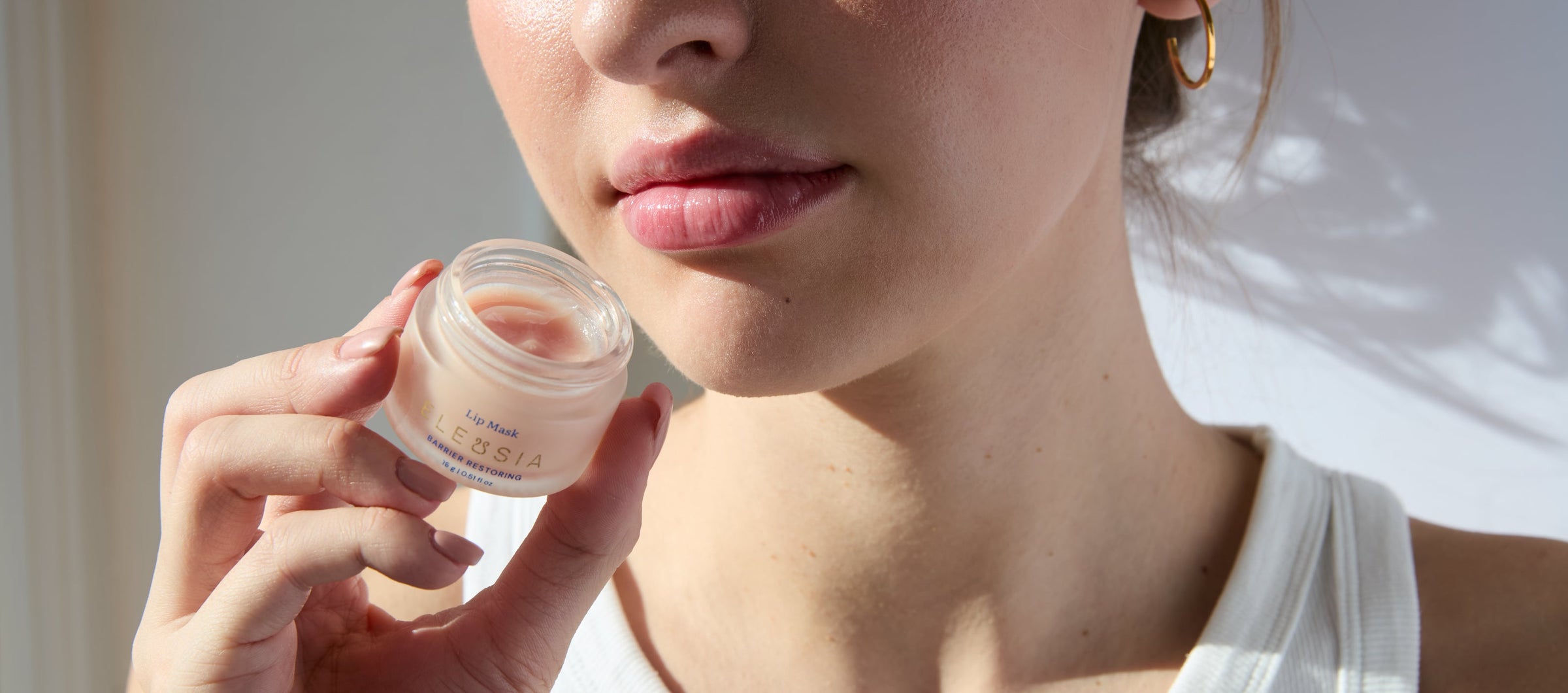 ELEUSIA Barrier Restoring Lip Mask in Greek Tea and Herbs product in hand, model holding open jar.