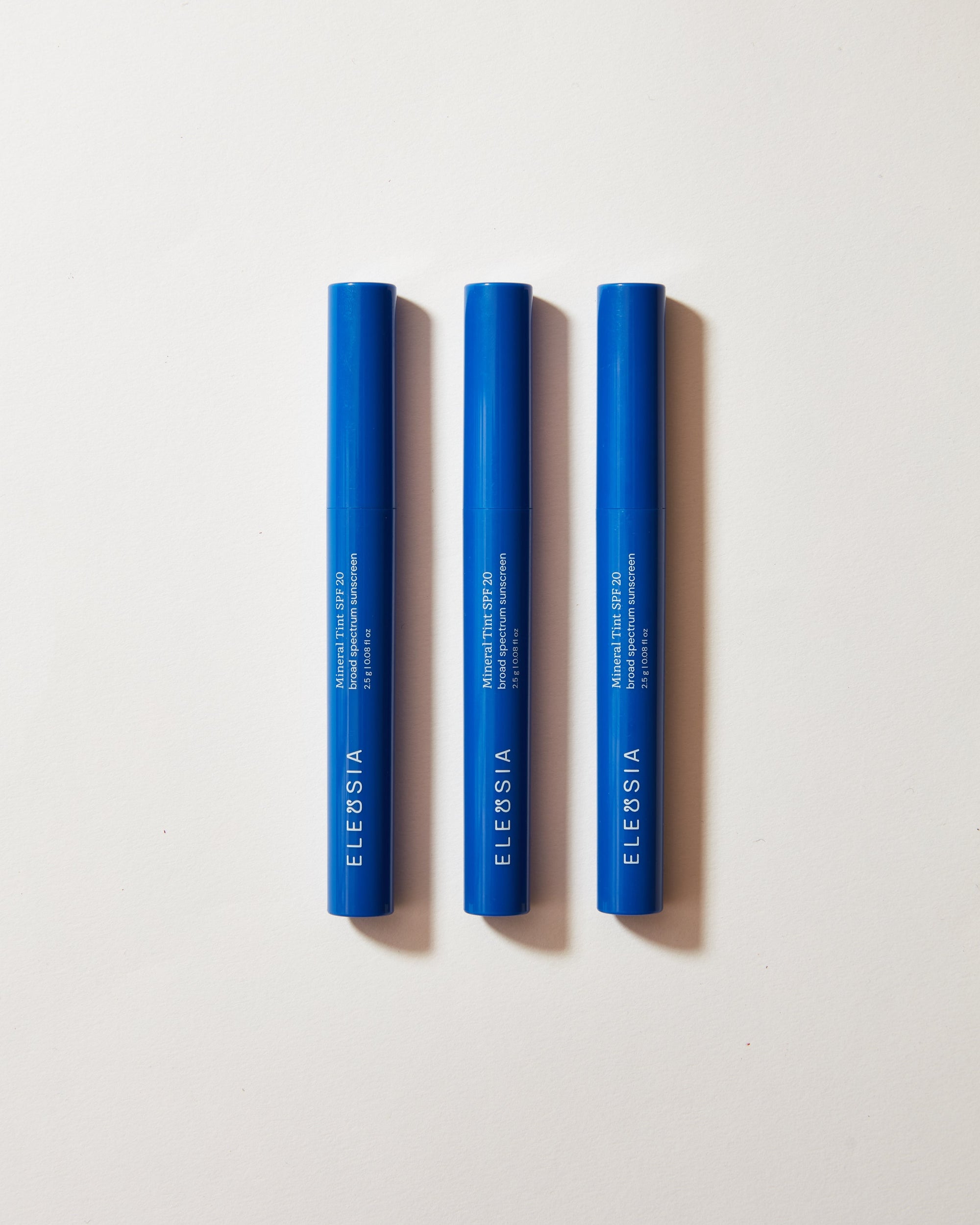 Three blue cosmetic tubes with 'Eleusia' branding on a light gray background